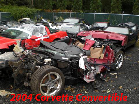 1976 Chevrolet Corvette - Multiple wrecked Corvettes are piled up in a junkyard, with the front of a red model prominently displayed.