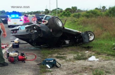 1976 Chevrolet Corvette - A black 1976 Chevrolet Corvette lies overturned on the side of the road, with emergency personnel and vehicles present.