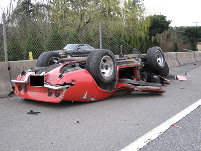 1976 Chevrolet Corvette - A red sports car is overturned on the side of the road, with debris scattered around it.