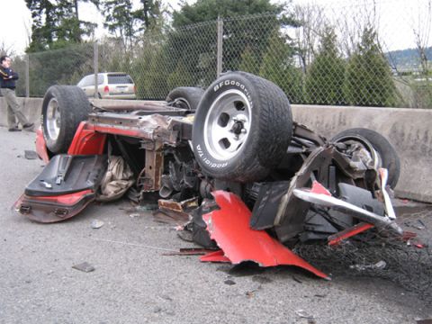 1976 Chevrolet Corvette - A red sports car lies overturned on the asphalt, its chassis mangled and wheels exposed.
