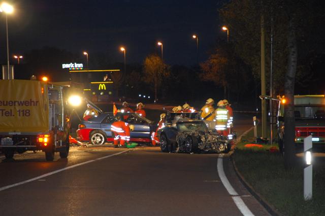 Wrecked dark blue sports car with front end damage, firefighters present