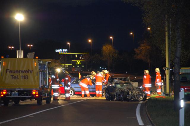 Wrecked black sports car and blue sedan with emergency responders at night