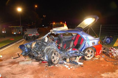 1976 Chevrolet Corvette - A severely damaged blue hatchback sits on a road at night, with debris scattered around it. Another vehicle is visible in the background.