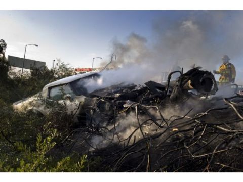 1976 Chevrolet Corvette - A severely damaged white vehicle is seen smoking heavily, with emergency personnel present at the scene.