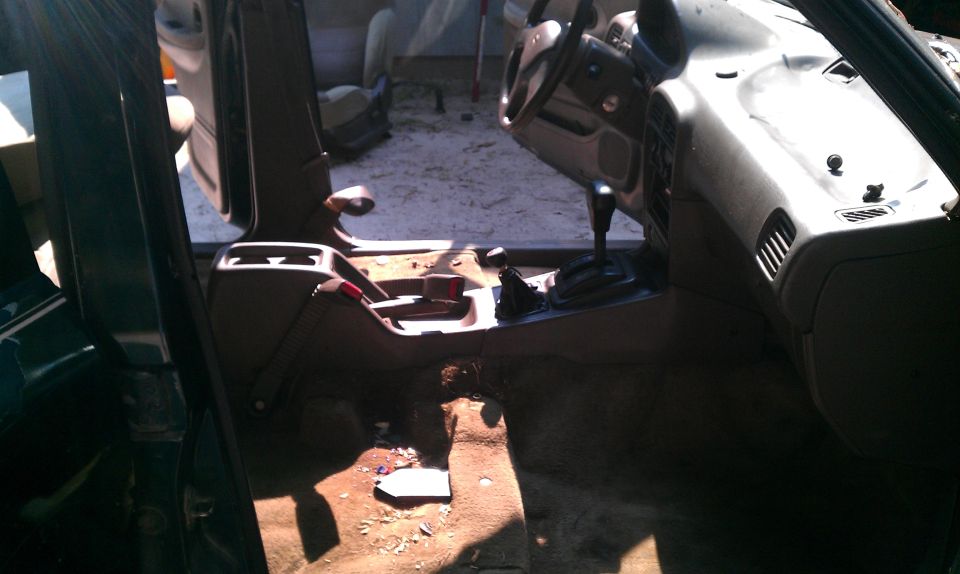 Disassembled tan car interior with manual shifter, console, and missing driver seat