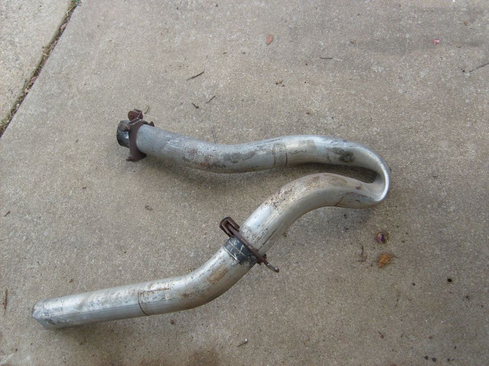 Two bent exhaust pipes on concrete, one with a clamp