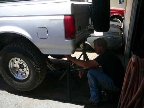 1988 Ford Bronco - Man works on the rear suspension of a 1988 Ford Bronco, which is supported by jack stands.
