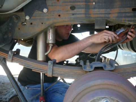 1988 Ford Bronco - A mechanic works on the underside of a vehicle, attending to the suspension system.