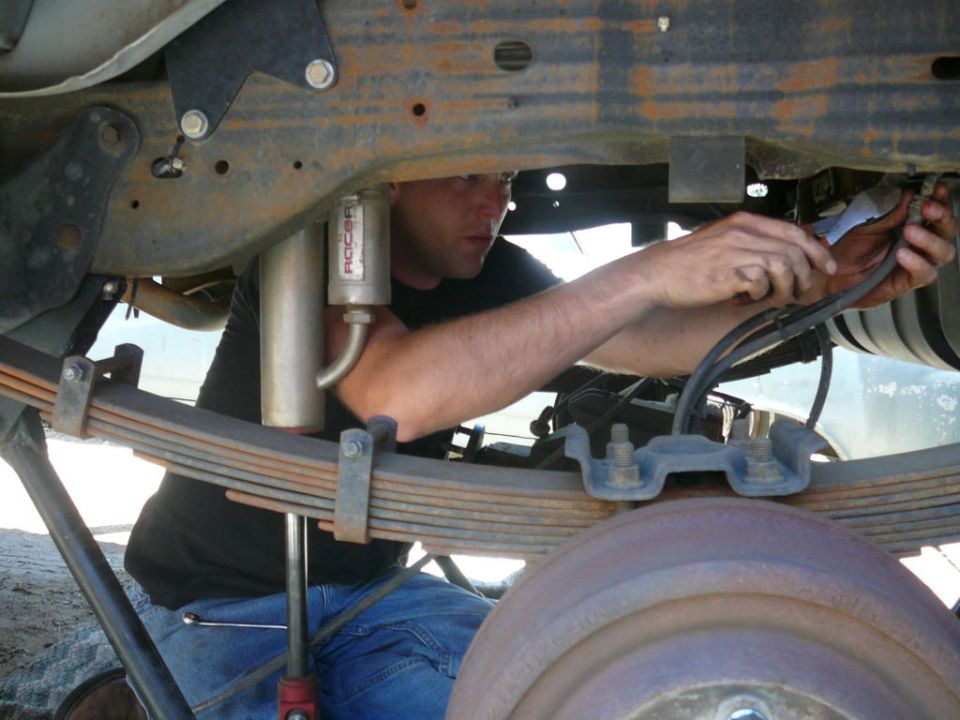 Man working on the rear suspension of a vehicle, focusing on leaf springs and a shock absorber