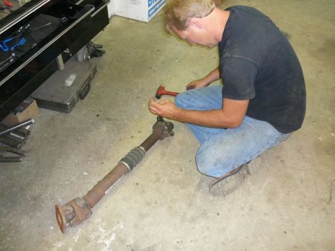 1988 Ford Bronco - A mechanic works on a vehicle's driveshaft, which is lying on the garage floor.
