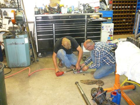 1988 Ford Bronco - Mechanics are seen working on car parts in a garage environment.