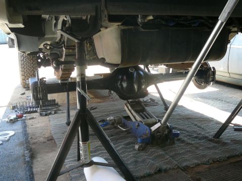 1988 Ford Bronco - Vehicle's rear axle and suspension components are visible, supported by jack stands and a floor jack for maintenance.