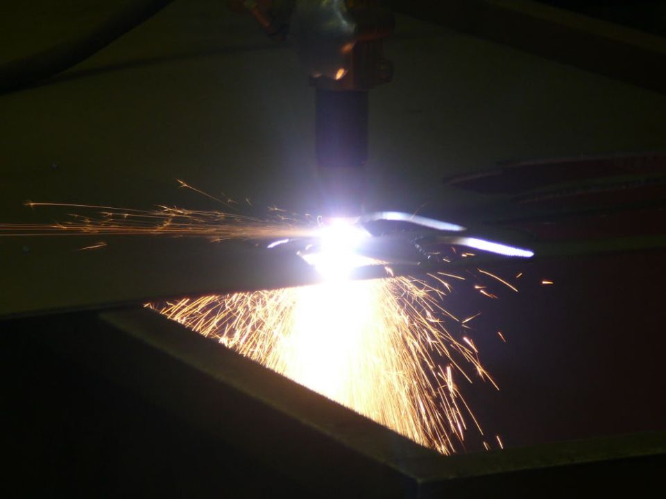 Plasma cutter creating sparks over metal, with "SUPERMOTORS" logo at bottom right