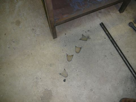 1988 Ford Bronco - Four metal brackets are scattered on a concrete floor next to a metal rod and a wooden workbench.