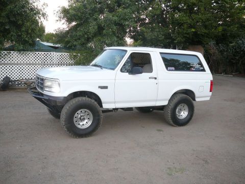 1988 Ford Bronco - This white Ford Bronco features an aftermarket bumper and large tires, suggesting a modified build.