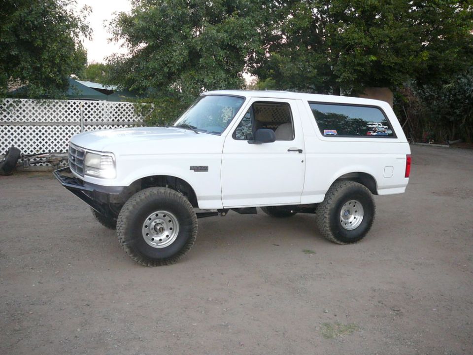 White Ford Bronco with aftermarket bumper and large tires, side view