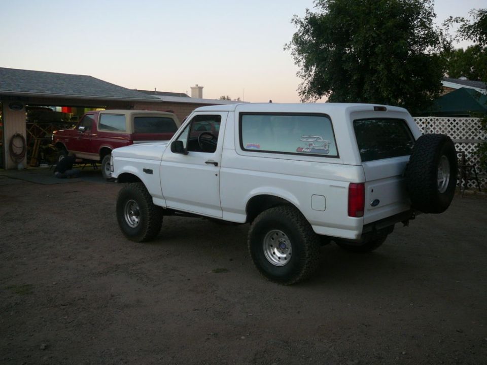 White Ford Bronco parked outside, another red Bronco visible under carport