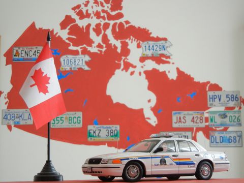 1999 Lincoln Town Car - A model police car sits in front of a map of Canada adorned with various license plates, accompanied by a small Canadian flag.