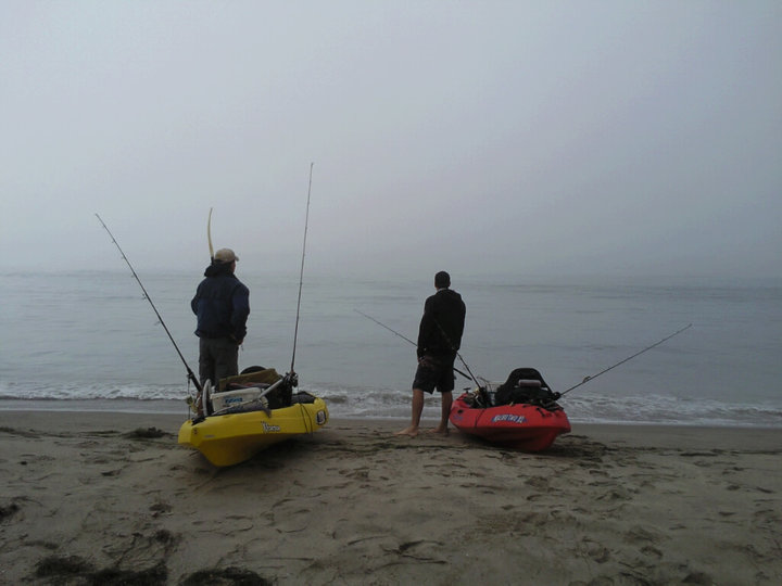 Yellow and red kayaks with fishing rods on a sandy beach with two people