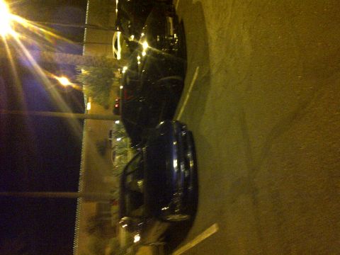 1995 Ford Probe - Two cars are parked on the side of the road at night under streetlights.