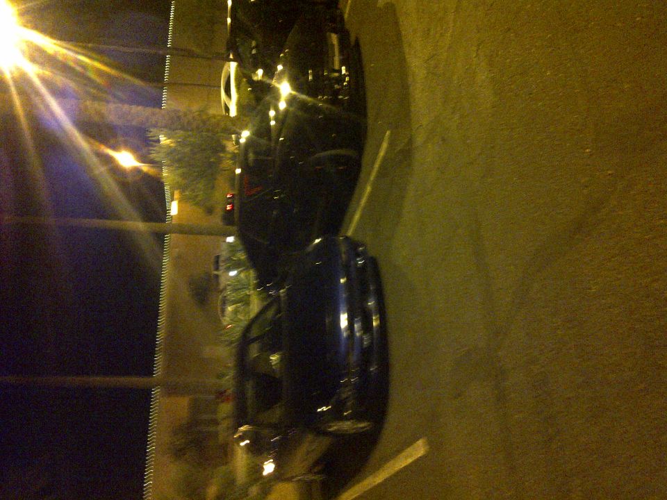Two dark cars parked on a street at night, one in front of the other