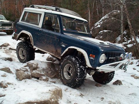 1977 Ford Bronco - A blue 1977 Ford Bronco navigates a rocky, snow-covered trail, its off-road capabilities.