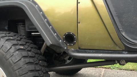 1974 Ford Bronco - Close-up of a Jeep Wrangler's side panel, aftermarket modifications like a fuel filler and fender flares.