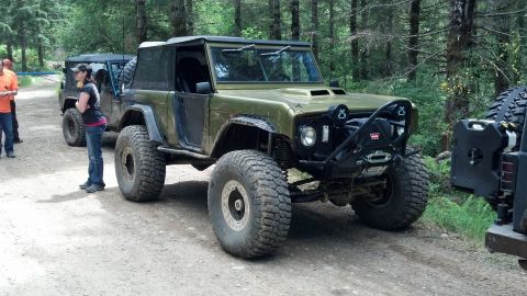 1974 Ford Bronco - A heavily modified Ford Bronco sits on a dirt road surrounded by trees, with another off-road vehicle behind it.