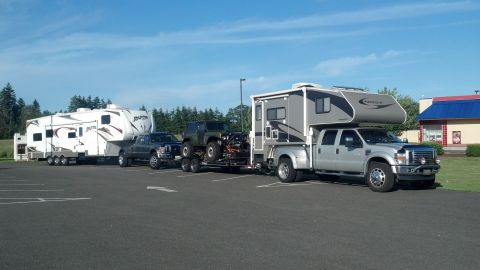 1974 Ford Bronco - A convoy of recreational vehicles, including a pickup with a camper and a jeep, and another pickup towing a large RV, parked in a lot.