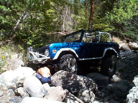 1977 Ford Bronco - 1977 Ford Bronco tackling a challenging rocky trail in a wooded area.