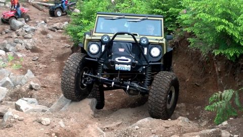 1974 Ford Bronco - Off-road vehicle tackling a challenging rocky path with ATVs in the distance.