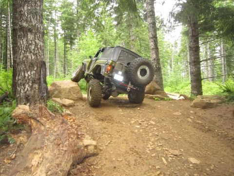1974 Ford Bronco - A modified off-road vehicle navigates a challenging rocky trail through a dense forest.