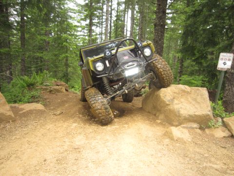 1974 Ford Bronco - An off-road vehicle navigates a challenging rocky terrain on a wooded trail.