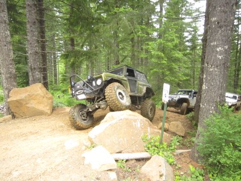 1974 Ford Bronco - Multiple off-road vehicles traverse a challenging forest trail with large boulders.