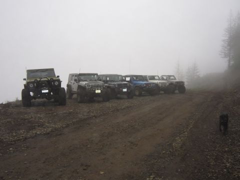 1974 Ford Bronco - A group of Jeeps are parked on a muddy, gravel road, partially obscured by fog.