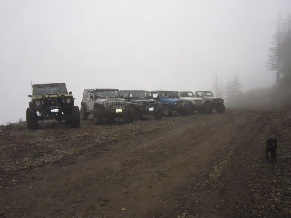 Several Jeeps parked on a dirt road with fog in the background