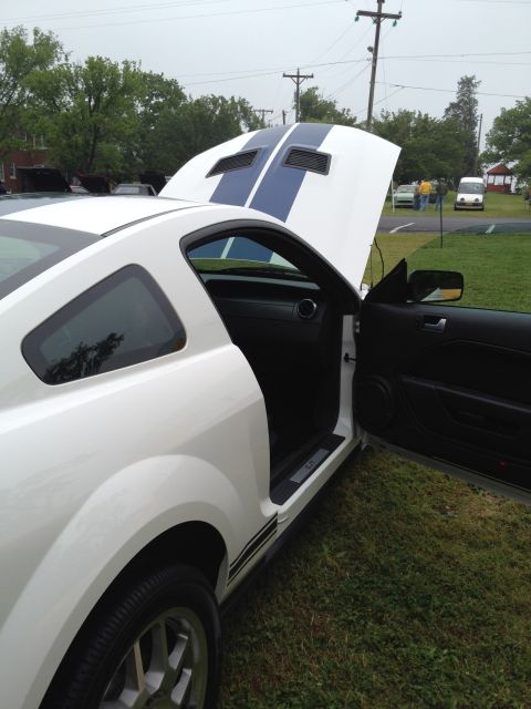 2007 Ford Mustang - White 2007 Ford Mustang coupe with hood and driver door open, displaying blue racing stripes on the hood.