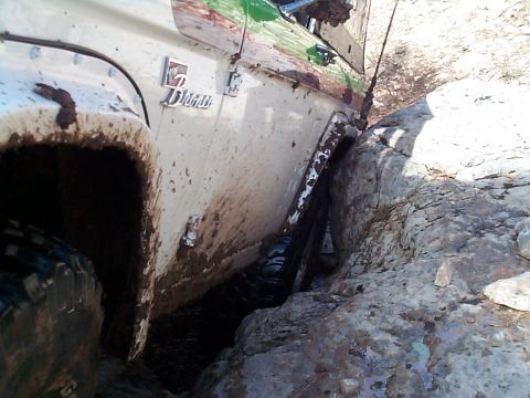 1977 Ford Bronco - A white 1977 Ford Bronco navigates a tight rocky passage, covered in mud.