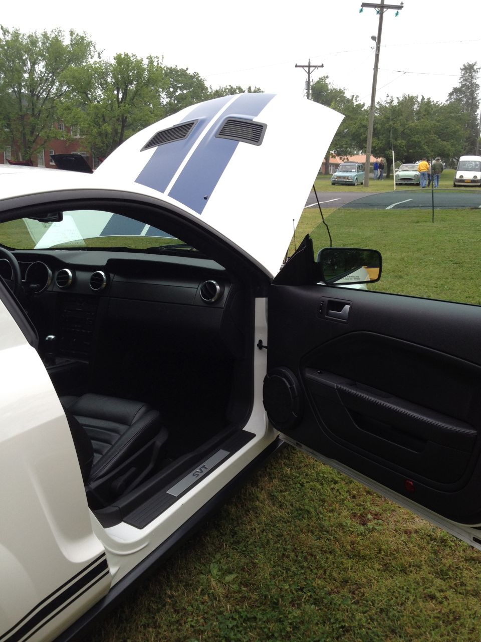 White 2007 Ford Mustang with blue stripes, open hood and driver's door, showing black interior and SVT door sill