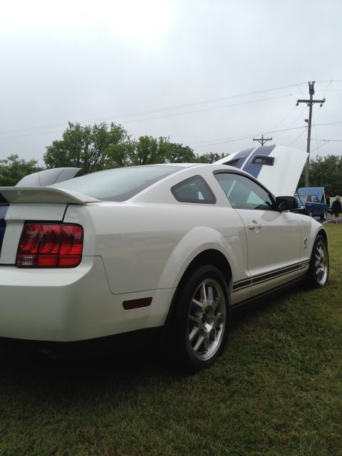 2007 Ford Mustang - White 2007 Ford Mustang coupe with racing stripes, hood open, parked on grass.