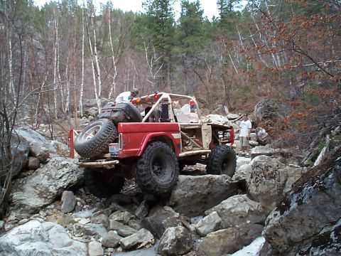 1977 Ford Bronco - A modified off-road vehicle tackles a challenging rocky path with two people visible.