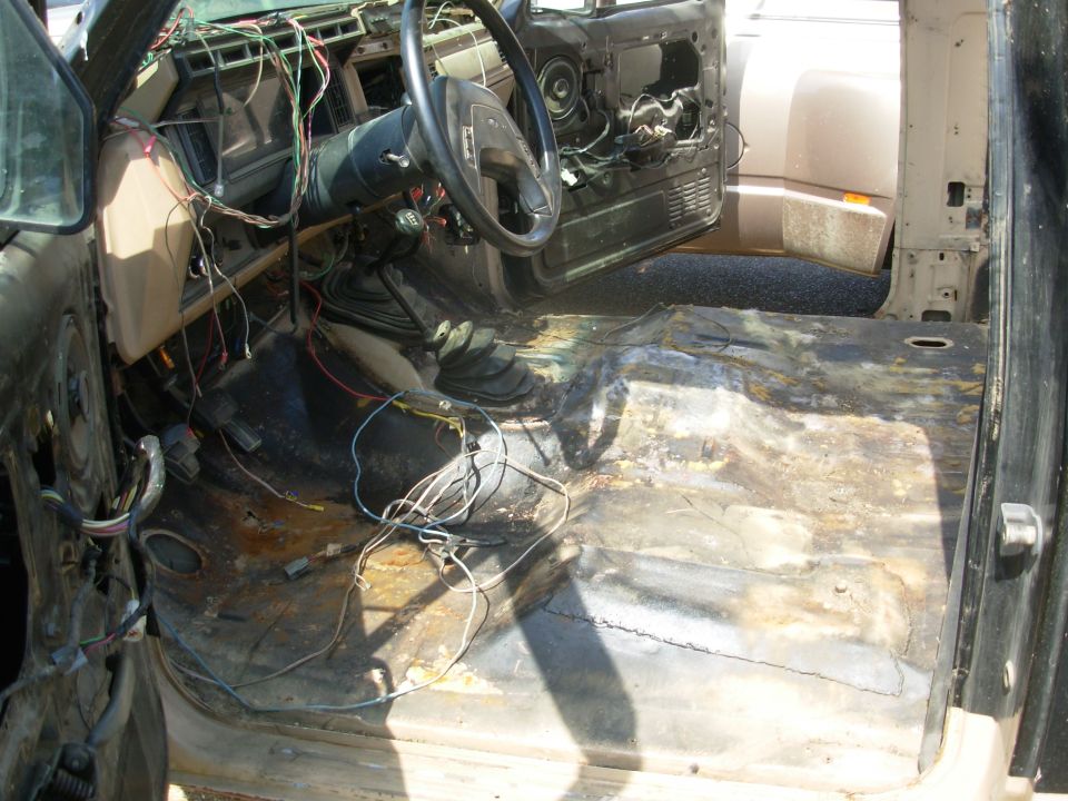 Stripped truck interior with exposed wiring, bare rusty floor, and dash removed