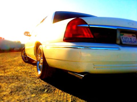 1999 Mercury Grand Marquis - Rear view of a white 1999 Mercury Grand Marquis, chrome accents and custom wheels under a bright sky.