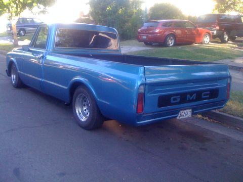1970 GMC C/K Pickup - This blue GMC pickup truck is shown from the rear, with other vehicles parked in the background.
