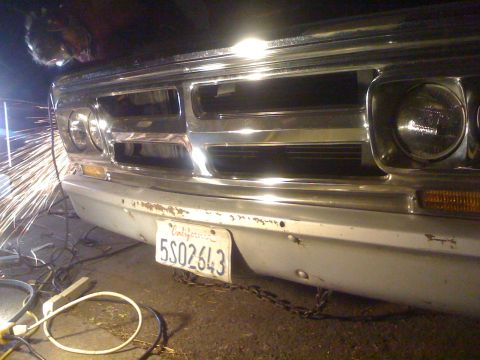 1970 GMC C/K Pickup - A close-up of a 1970 GMC C/K Pickup's front end shows a worker grinding near the bumper.