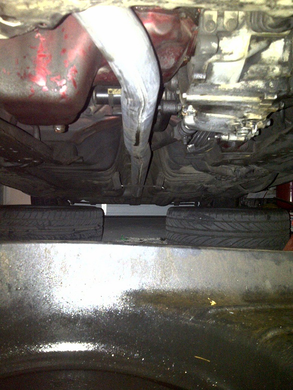 Underside view of a vehicle showing exhaust pipe, transmission, and tires on blocks
