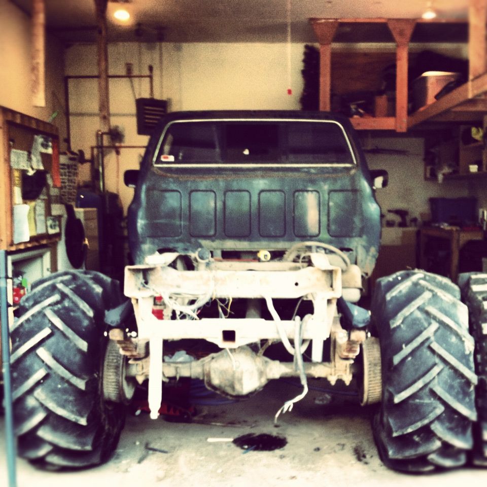Rear view of a monster truck with massive tires, stripped down chassis, in a garage