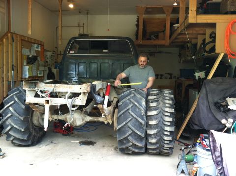 1983 Chevrolet C/K Pickup - A man measures a large tire next to a custom truck chassis that has been fitted with oversized tractor tires.