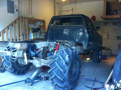 1983 Chevrolet C/K Pickup - A heavily modified pickup truck with oversized tires sits in a garage, undergoing repairs or customization.