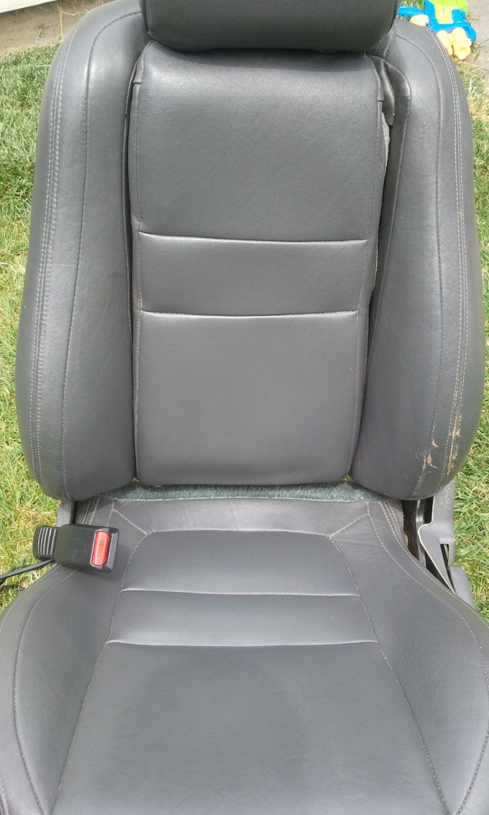 Gray leather car seat with visible wear on the side bolster and a seatbelt buckle
